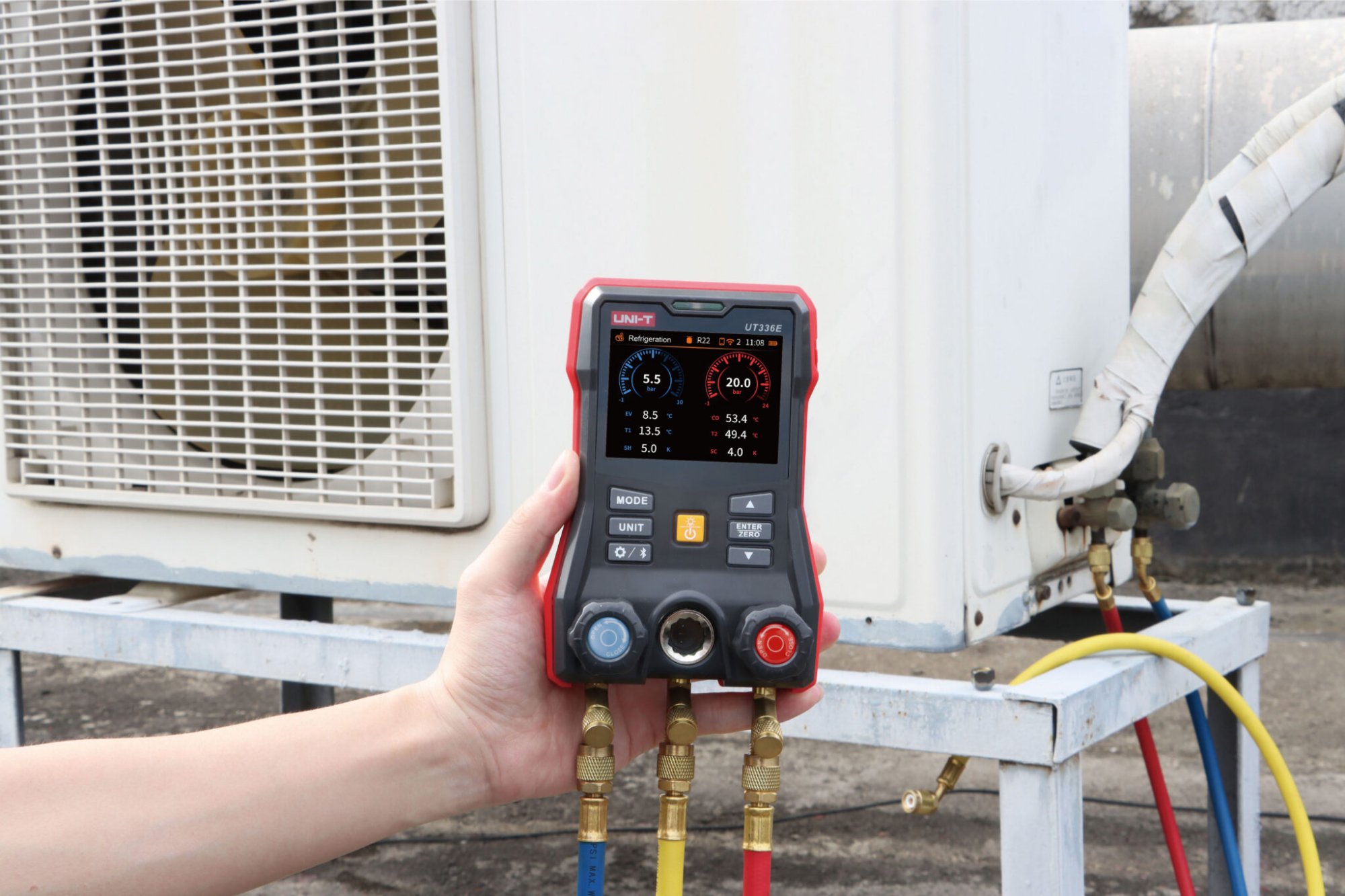 Technician holding the UT336E digital manifold connected to an outdoor HVAC unit
