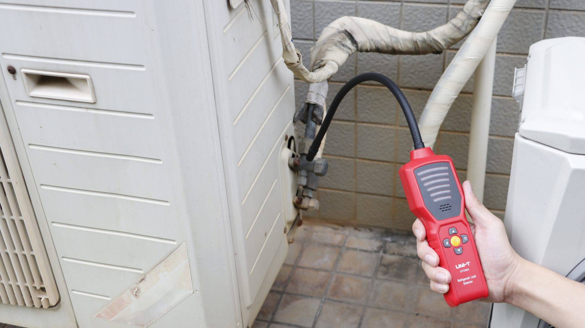 The UNI-T UT336A in use, detecting a refrigerant leak on the pipes of an outdoor air conditioning unit during maintenance.