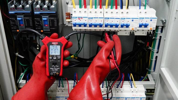 Spannungsmessung mit der UNI-T UT281F an einer Klemmleiste in einem Verteilerkasten, der Techniker trägt rote Schutzhandschuhe.