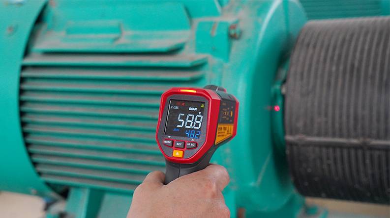 Hand holding the UNI-T UT305S infrared thermometer to measure the temperature of an industrial motor.