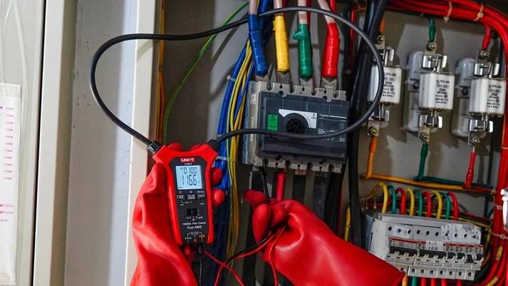 Die UNI-T UT281F wird zur Spannungsmessung mit Prüfspitzen an einem großen Schütz in einem industriellen Schaltschrank verwendet.
