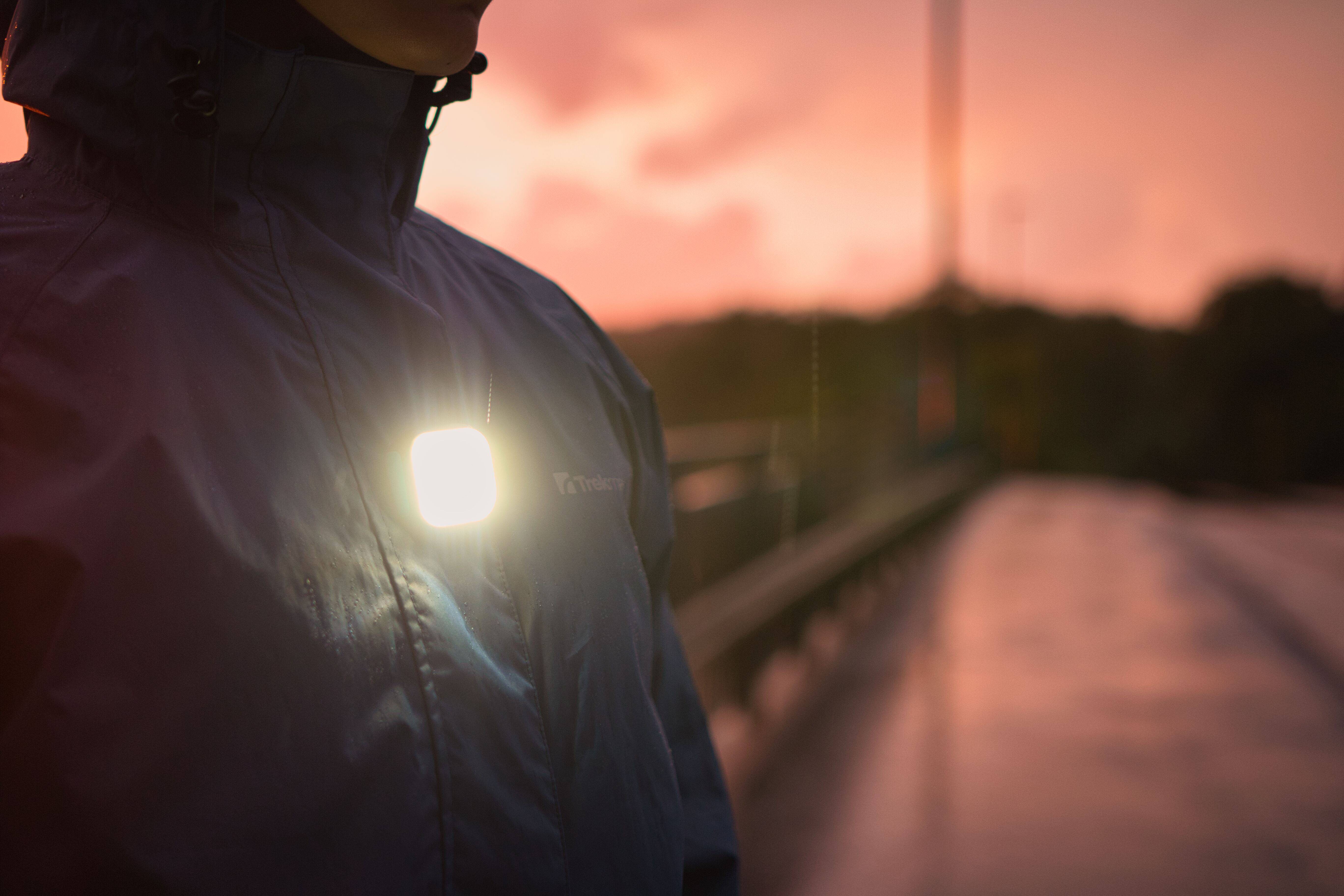 Person in einer Regenjacke trägt die MEOLINQ Light01 auf der Brust für Sichtbarkeit bei Dämmerung und schlechtem Wetter.