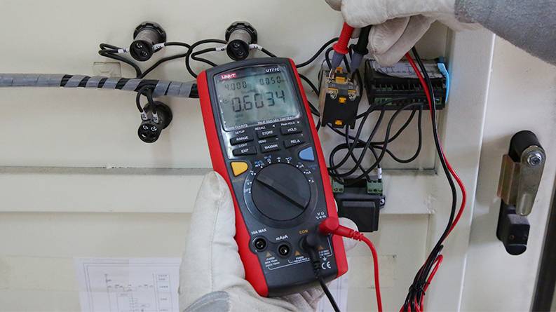 Das UNI-T UT71C True-RMS-Multimeter im professionellen Einsatz bei der Messung in einem Schaltschrank durch einen Techniker.